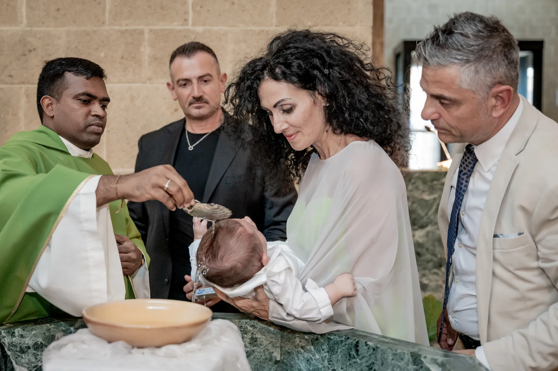 Il neonato riceve l’acqua del battesimo, sorretto dai familiari davanti al sacerdote