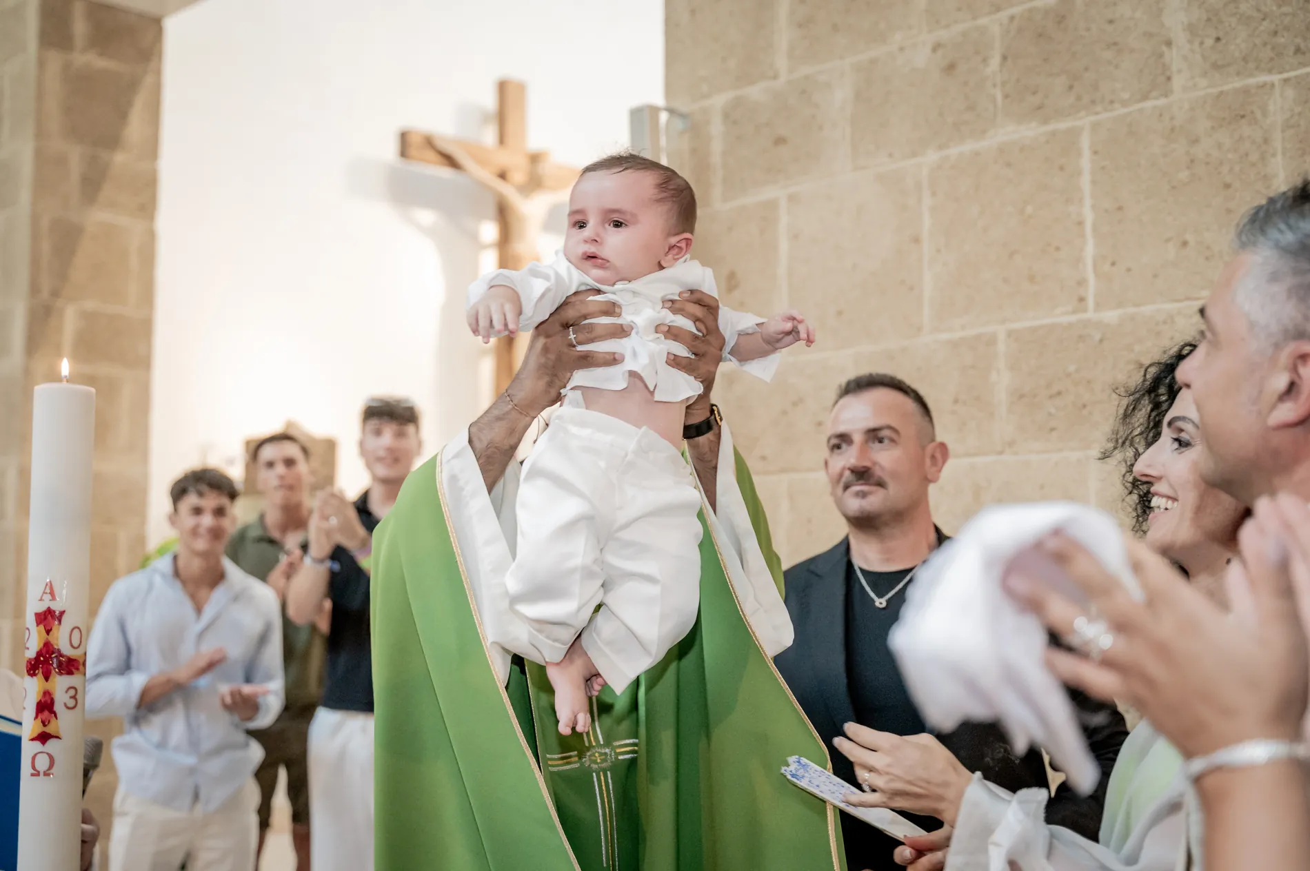 Il bambino sollevato dal sacerdote dopo il rito, tra gli applausi di parenti e amici