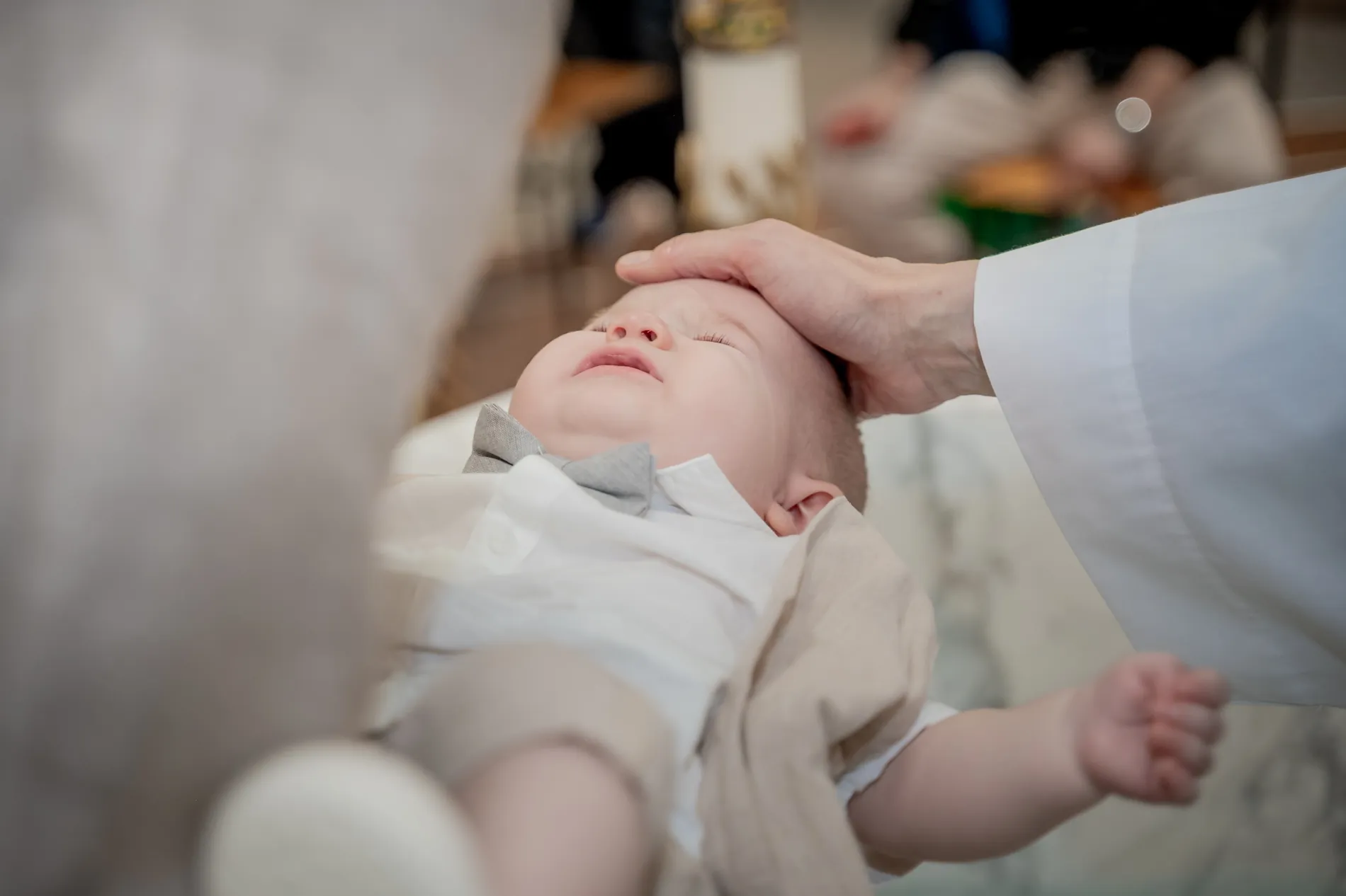 Il bambino dorme mentre il sacerdote gli posa una mano sulla testa per la benedizione