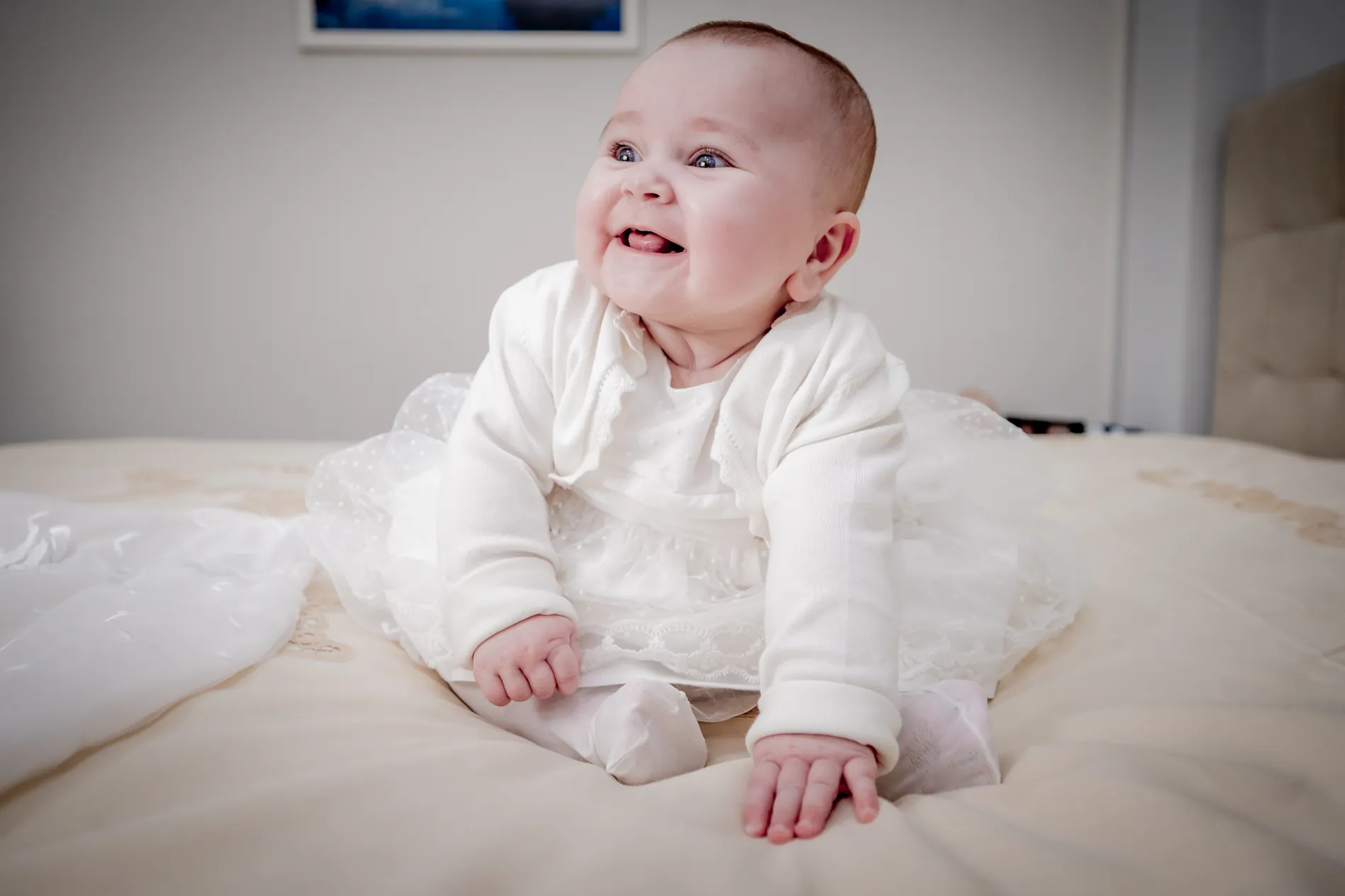 Primo piano di una neonata vestita di bianco che sorride, seduta sul letto
