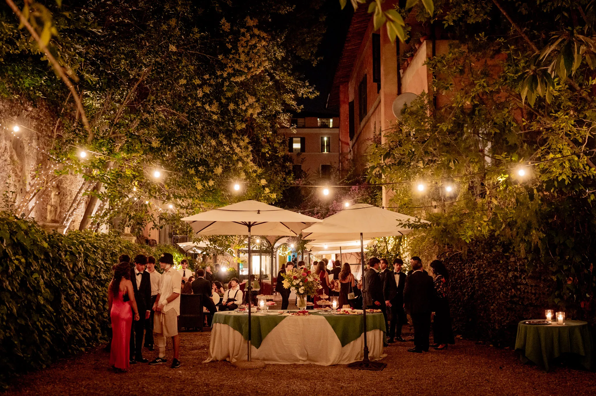 Invitati a una cena serale in giardino, tra ombrelloni e filari di lucine