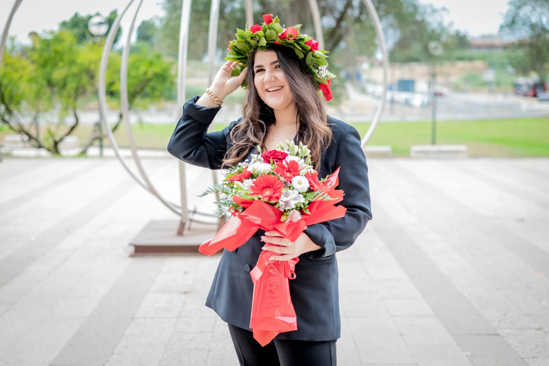 Neolaureata all’aperto con una mano sulla corona d’alloro e un mazzo di fiori rossi e bianchi