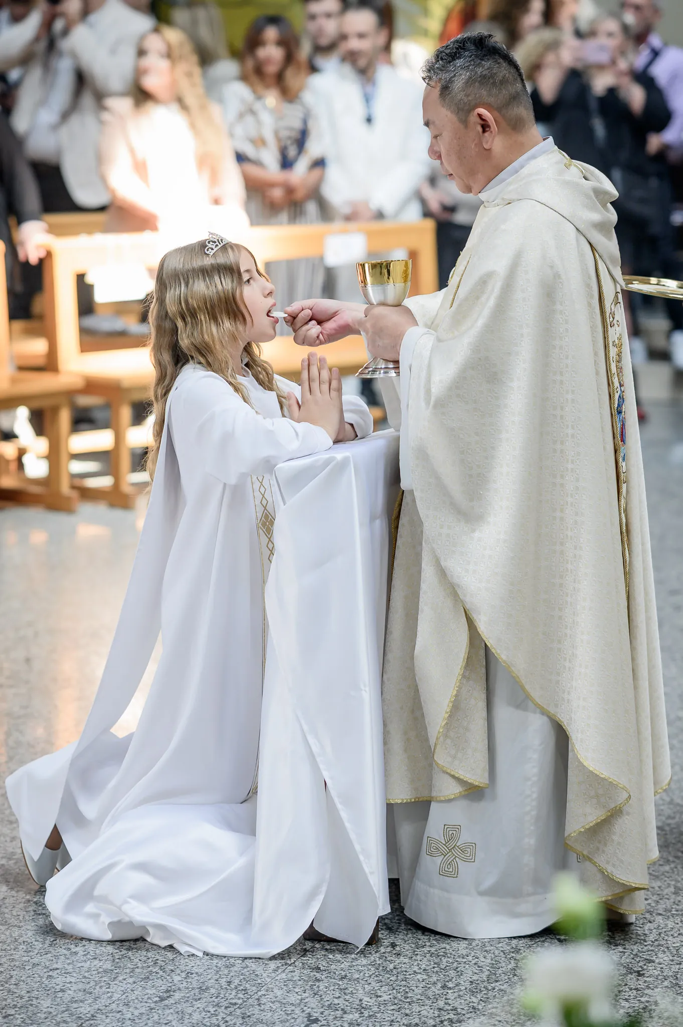 Il sacerdote porge la comunione alla bambina con la tunica bianca