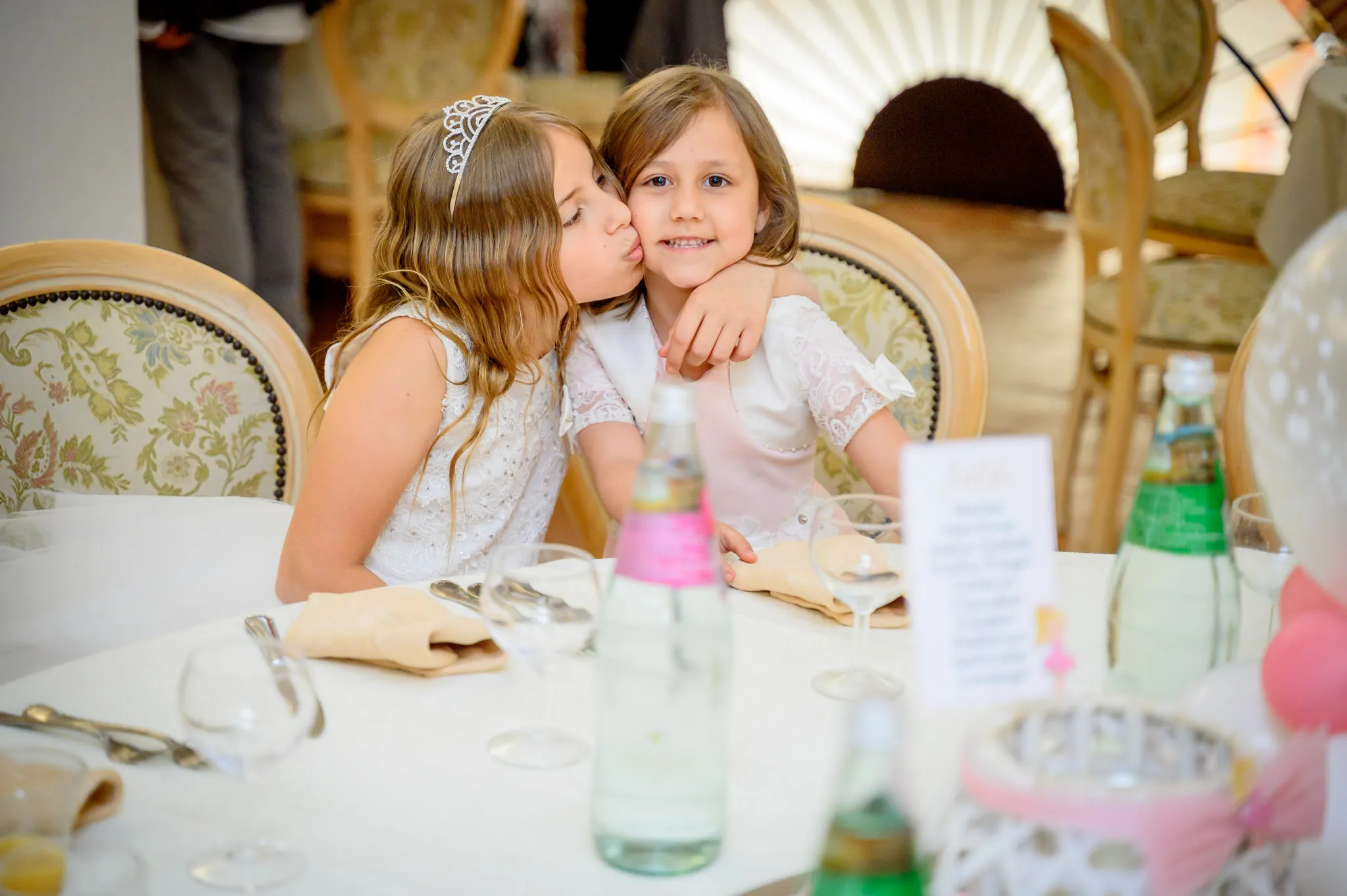 Un bacio sulla guancia tra la bambina con la coroncina e un bimbo, seduti a tavola