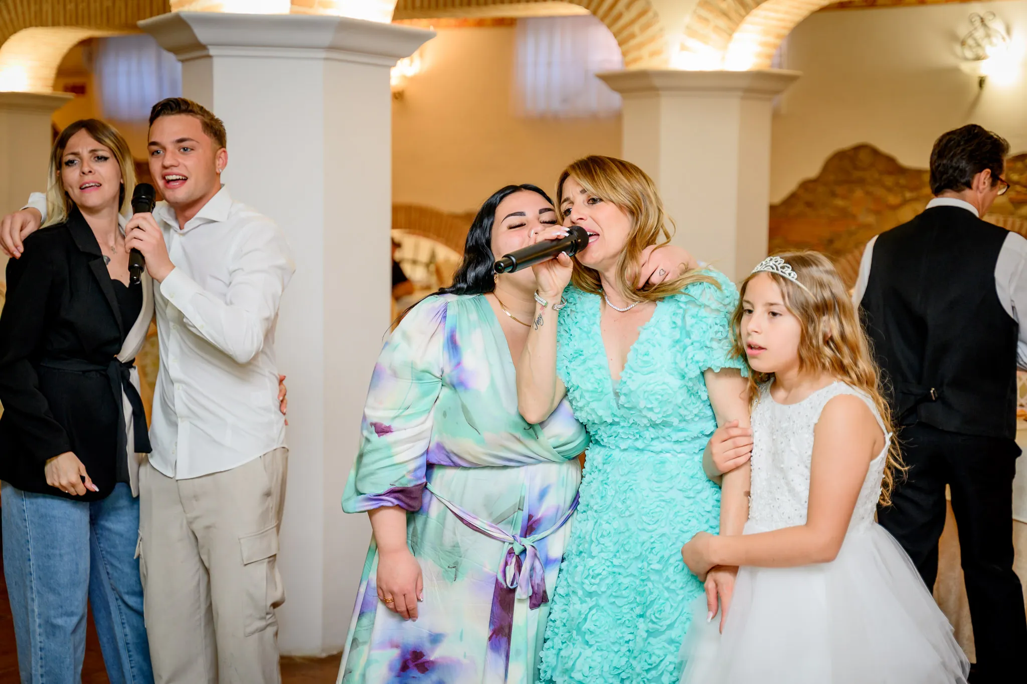 Due donne cantano al microfono accanto alla bambina della prima comunione