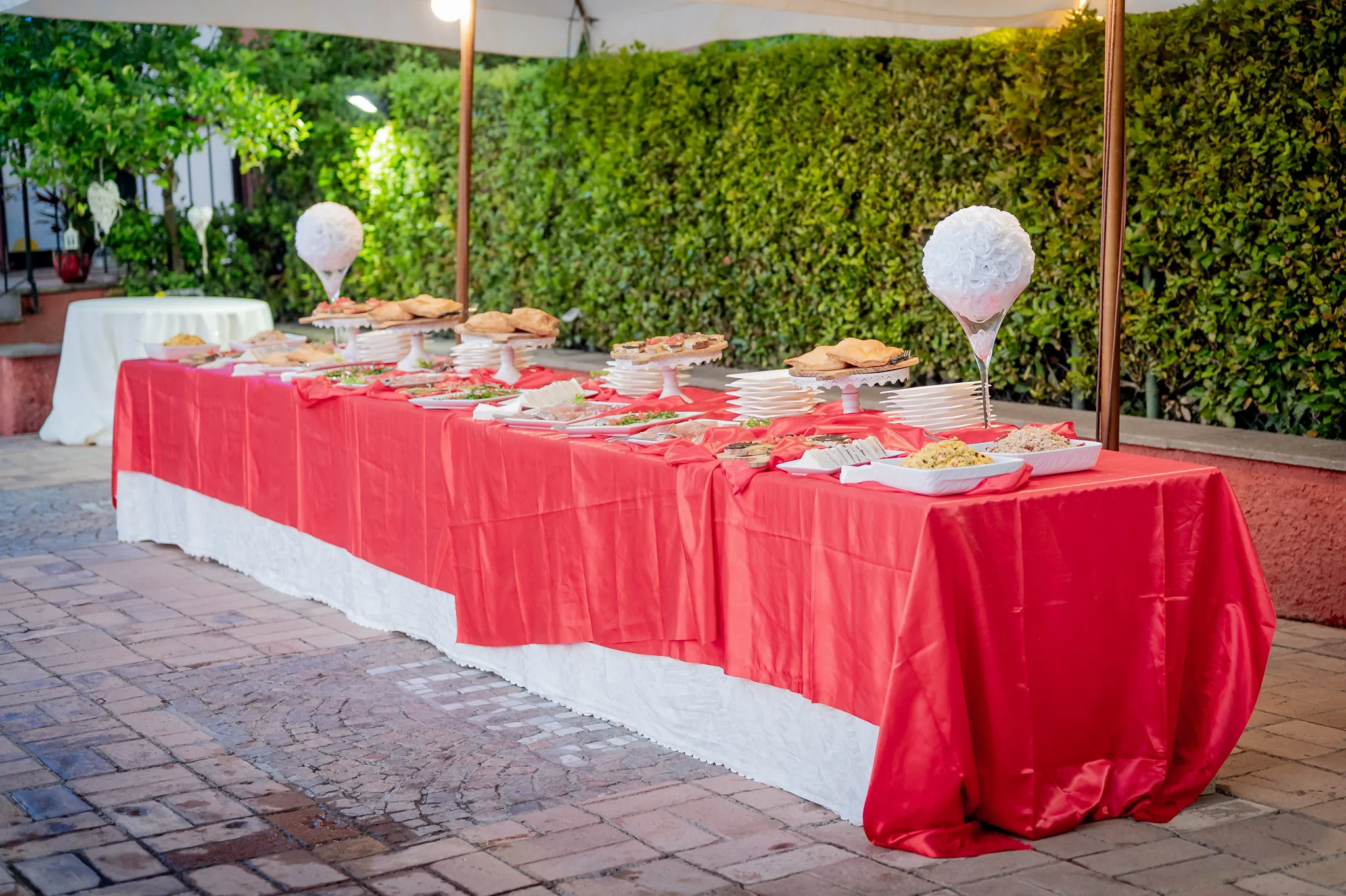 Lungo tavolo del buffet con tovaglia rossa sotto un pergolato