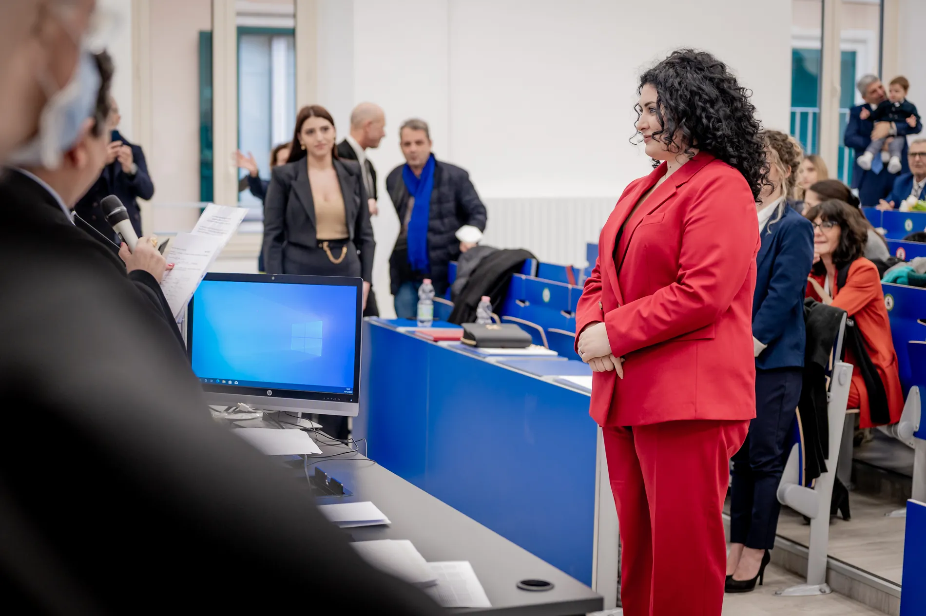 Discussione della tesi davanti alla commissione, con la laureanda in rosso accanto alla postazione
