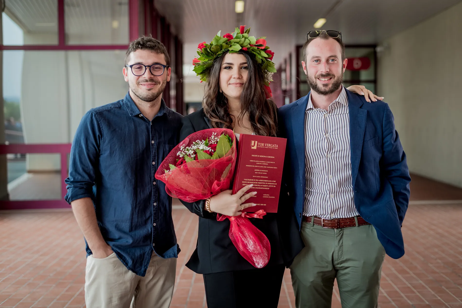 Foto ricordo con due amici davanti all’aula, con la tesi e il bouquet