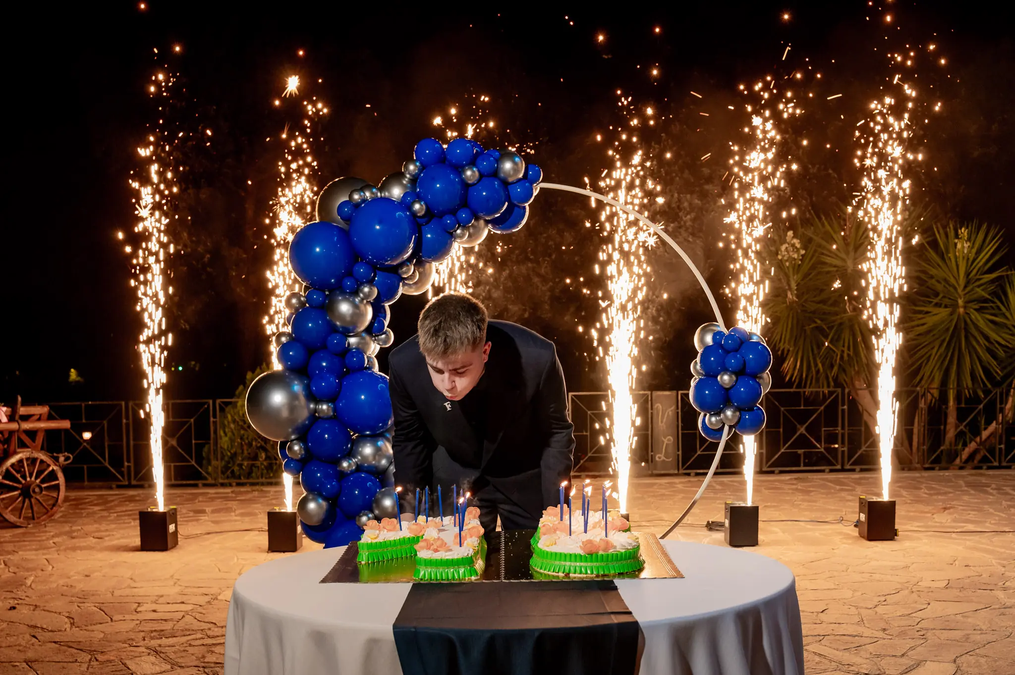 Il festeggiato soffia sulle candeline tra le fontane di scintille e l’arco di palloncini blu