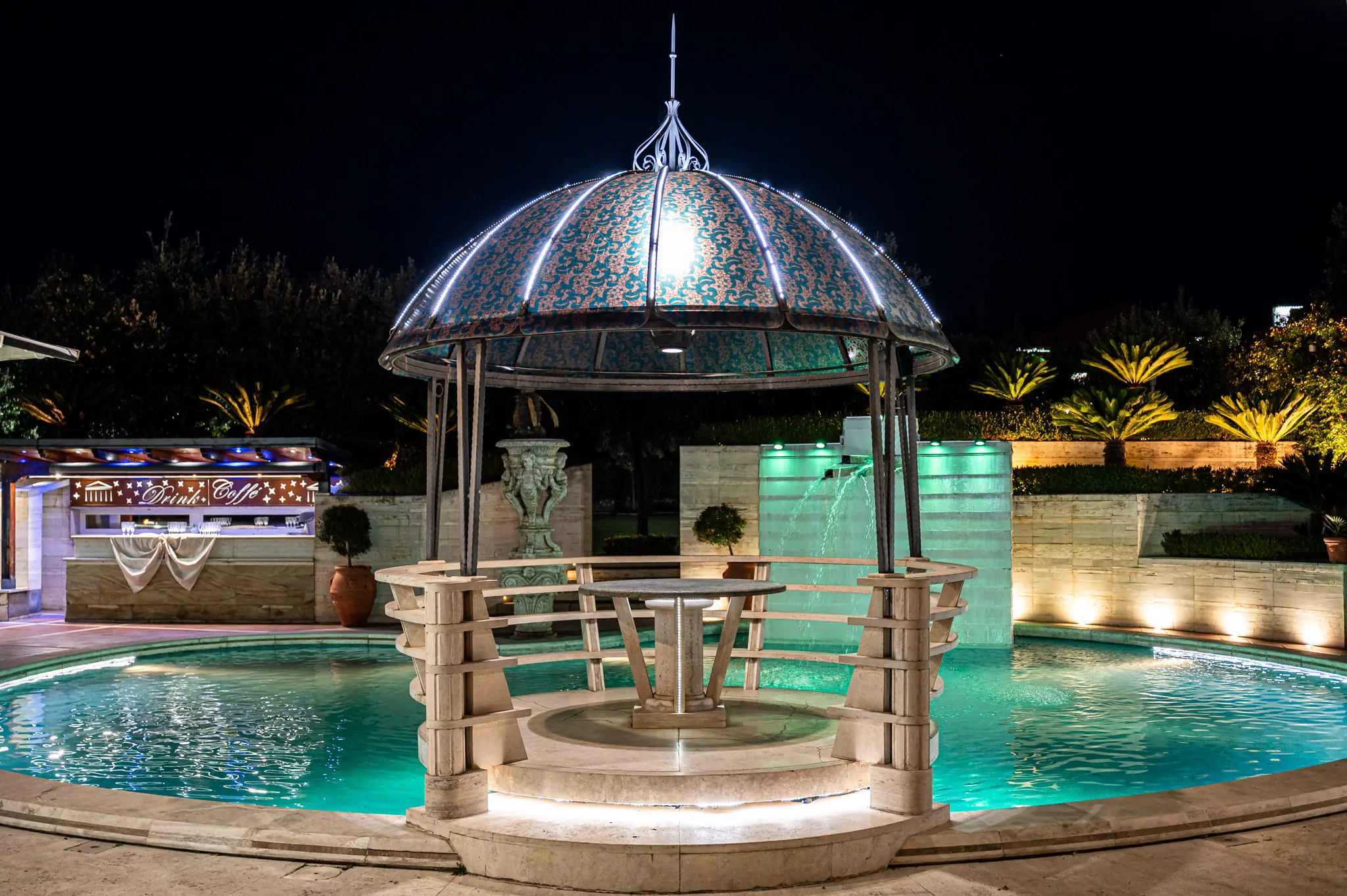 Gazebo in ferro battuto al centro di una piscina illuminata di notte